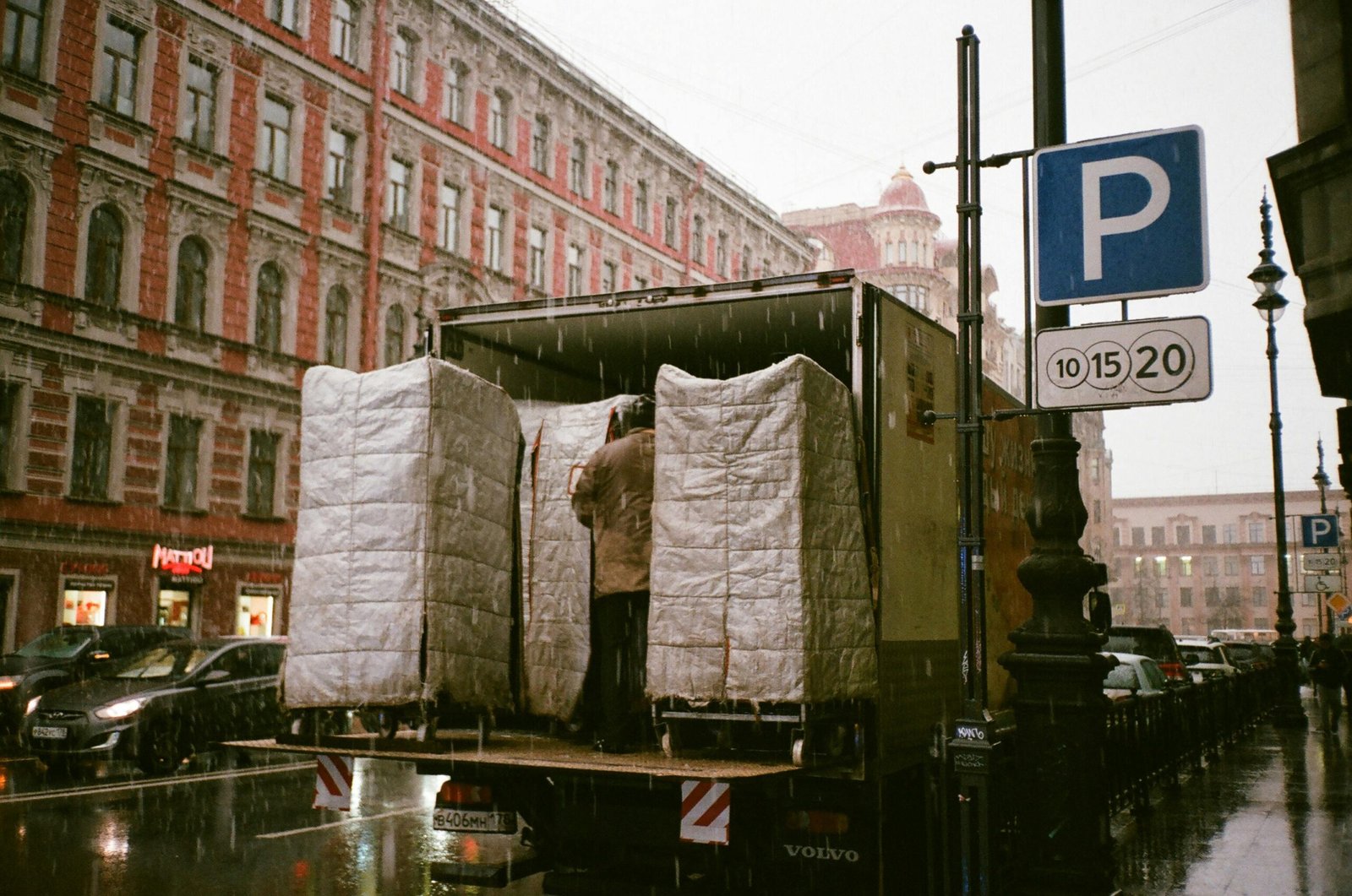 A truck being loaded on a rainy urban street, reflecting city life and transportation.
